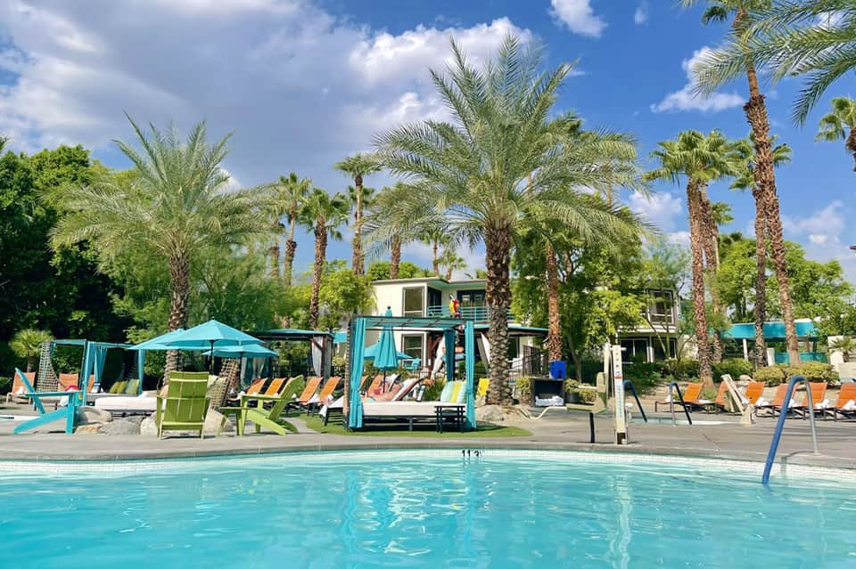 Resort pool with turquoise water, palm trees, lounge chairs, and modern cabana structures