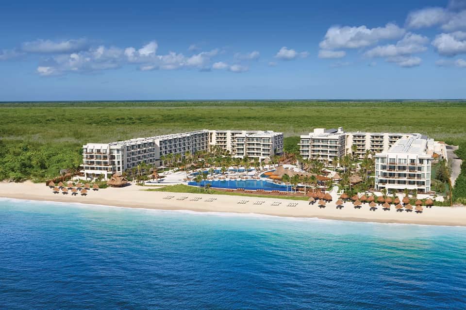 Aerial view of beachfront resort with blue pool, sand, and multi-story buildings