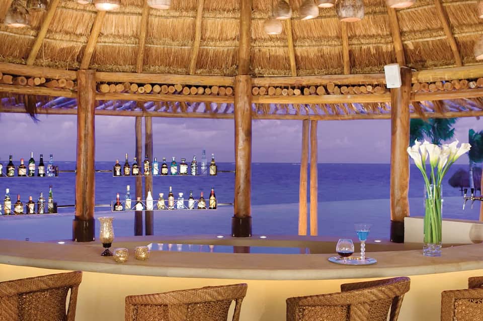 Beachfront tiki bar with ocean view and illuminated shelves of liquor