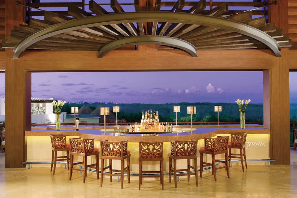 Elevated bar with wooden chairs overlooking scenic landscape at twilight with ambient lighting