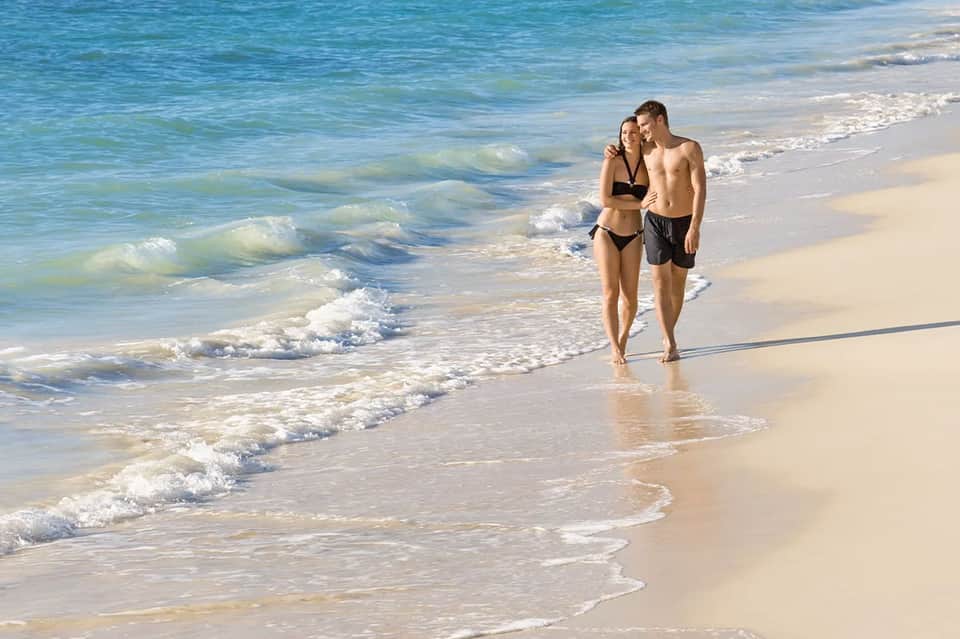 Couple walking along sandy beach with waves and blue ocean water in background