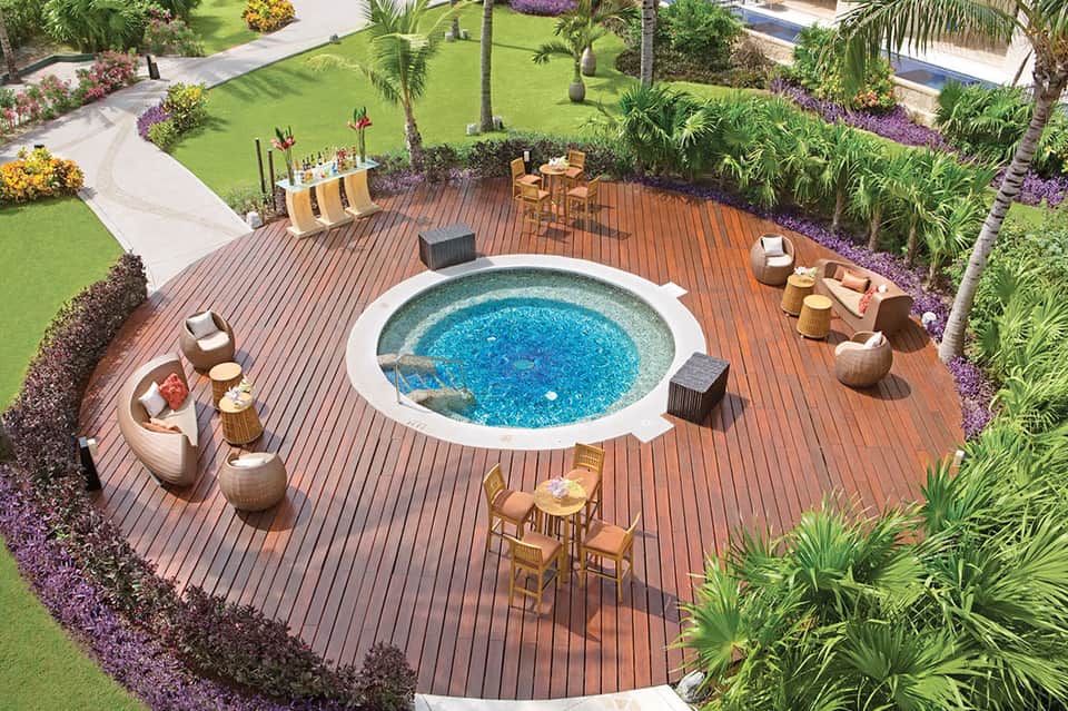 Aerial view of circular hot tub on wooden deck surrounded by landscaped gardens and palm trees