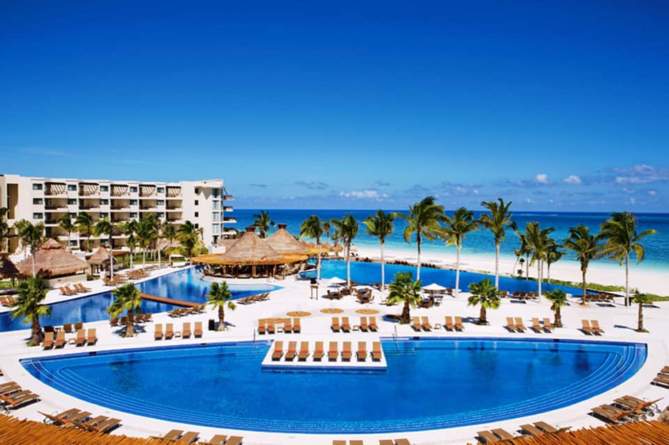 Beachfront all-inclusive resort with curved infinity pool, palm trees, and ocean view in tropical setting