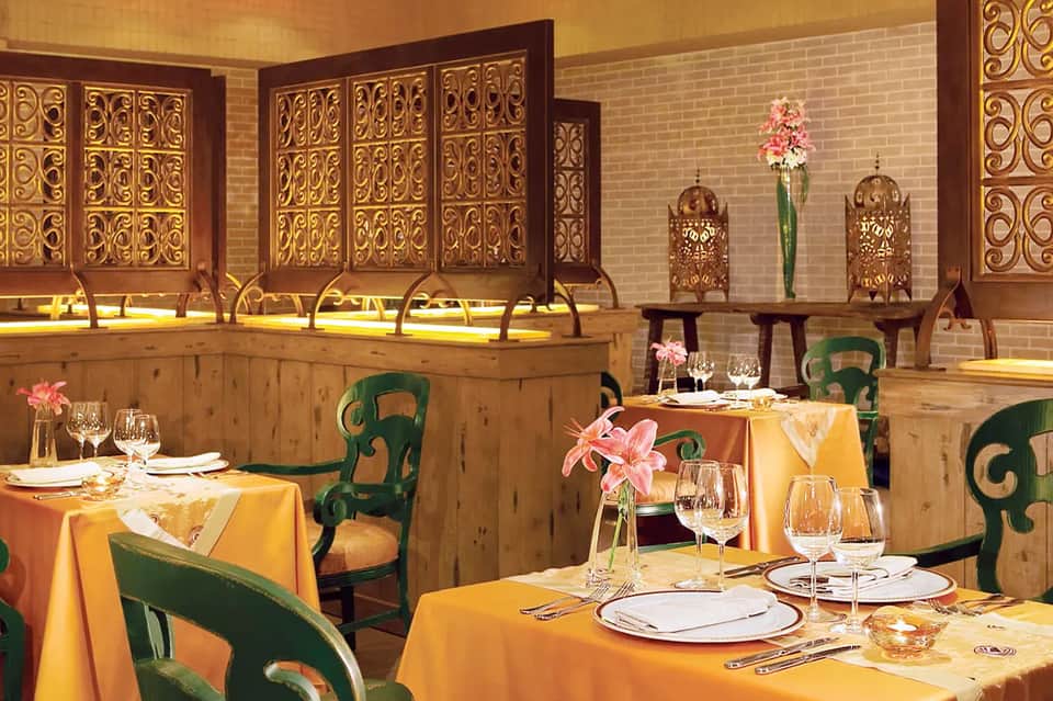 Upscale restaurant interior with golden decorative panels, green chairs, and elegant yellow tablecloths