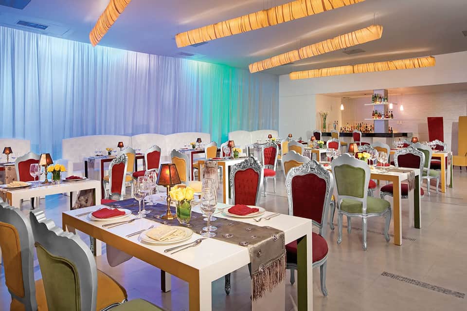 Upscale restaurant dining room with colorful chairs, elegant table settings, and ambient lighting