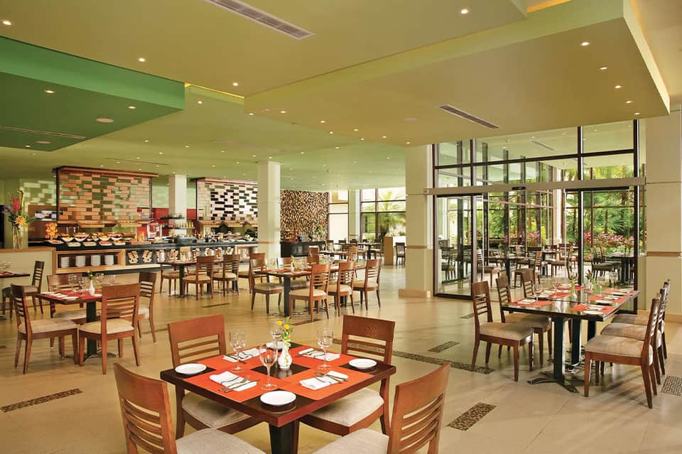Modern resort dining room with buffet stations, tables, and garden views through glass doors