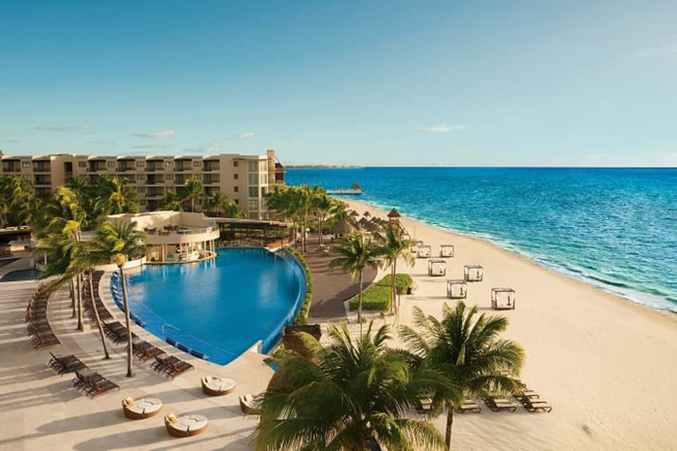 Beachfront resort with heart-shaped pool, palm trees, sandy beach, and ocean view