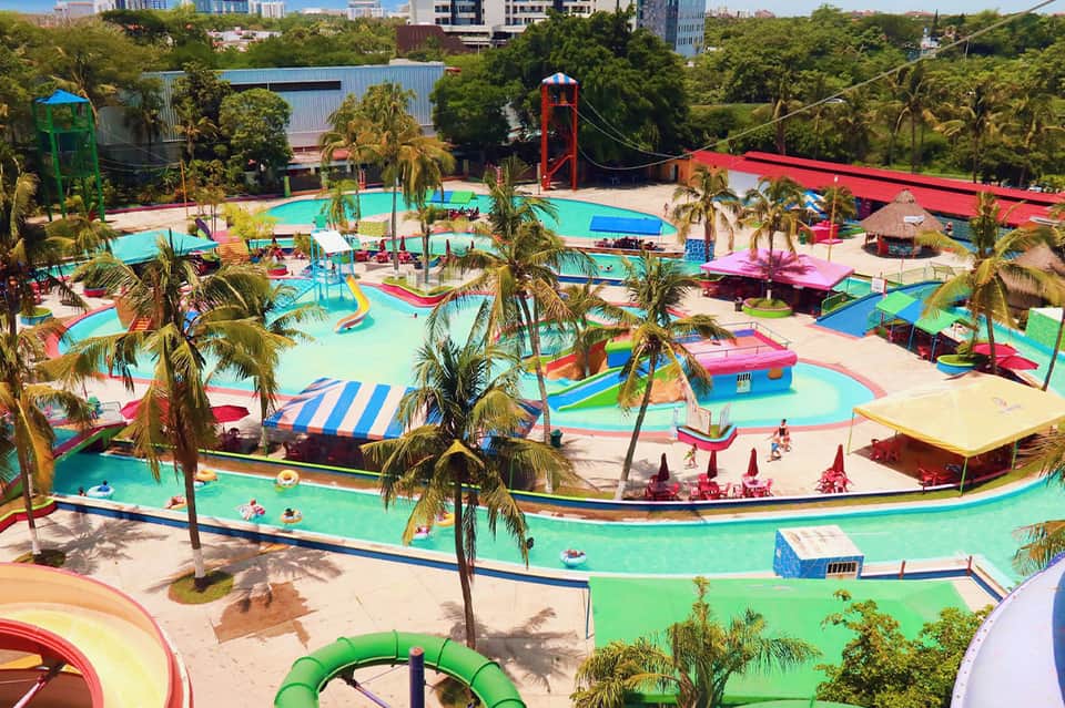 Colorful lazy river water park with vibrant pink, blue, and green pools, slides, and palm trees