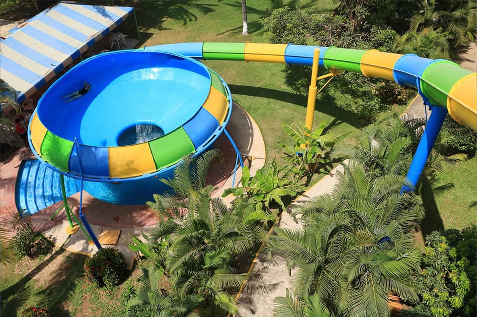 Colorful water slide and trampoline in resort pool surrounded by green lawn and palm trees