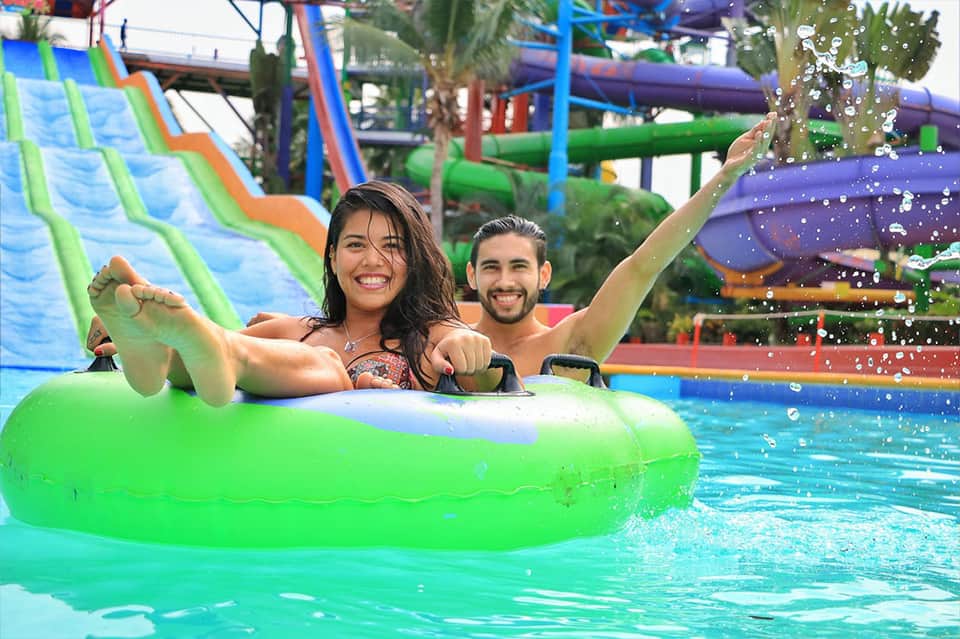 Couple on bright green water raft with colorful slides in background at water park