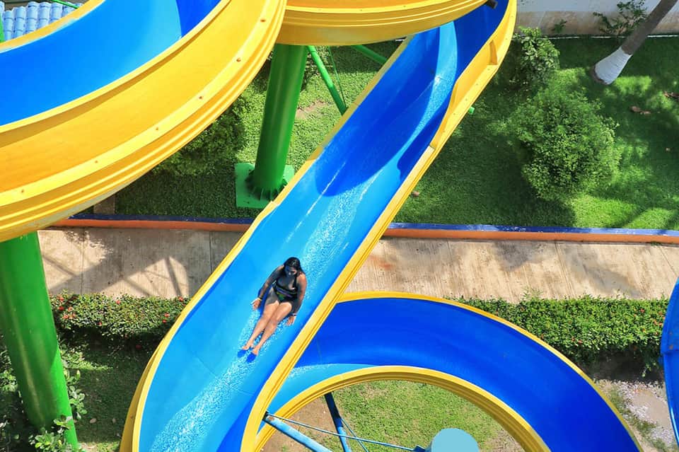 Woman sliding down bright blue and yellow water slide at outdoor water park