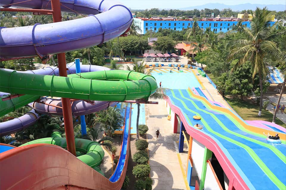 Aerial view of colorful water slides and pools at tropical resort surrounded by palm trees