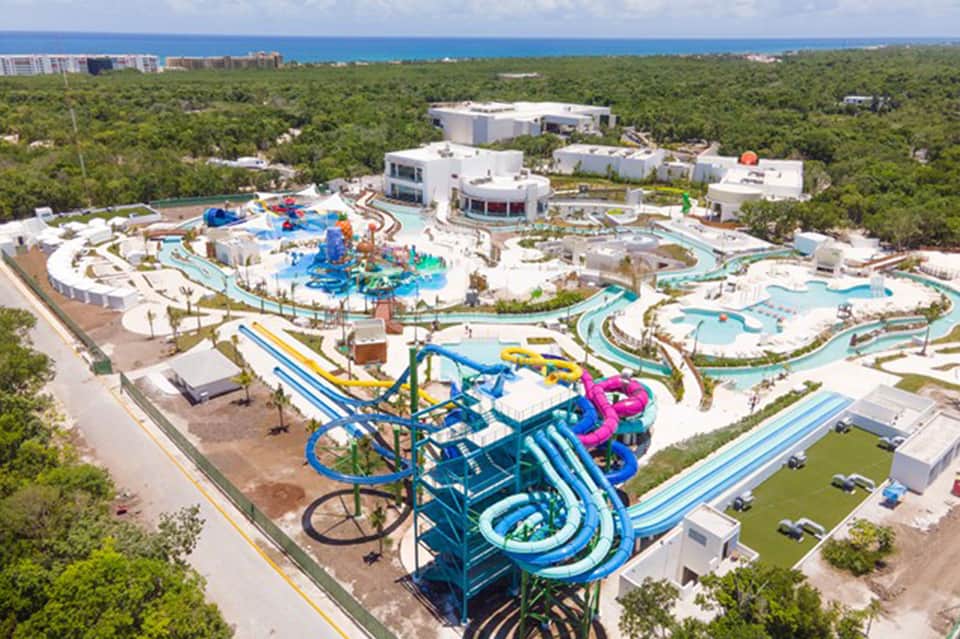 Aerial view of large water park resort with colorful slides, pools, and surrounding forest near ocean