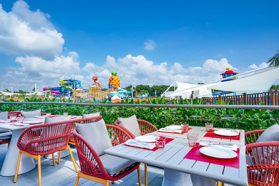 Outdoor dining terrace with red chairs overlooking colorful water park attractions and green landscaping