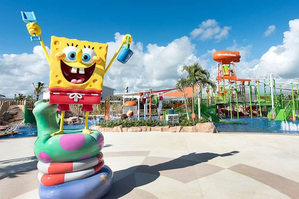 SpongeBob SquarePants statue at colorful water park with slides and palm trees