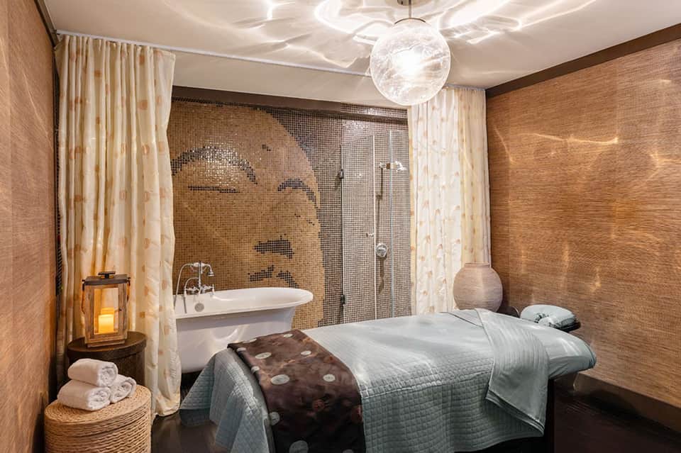 Spa treatment room with massage bed, soaking tub, and natural stone finishes
