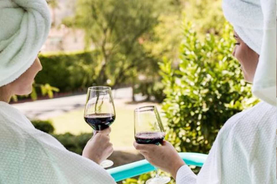 Two people toasting with red wine glasses overlooking pool and tropical garden setting