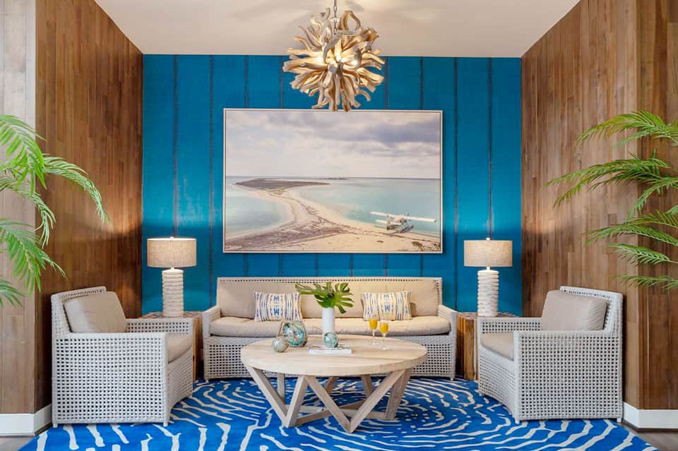 Coastal-themed living room with turquoise accent wall, beige sofa, beach photograph, and plants