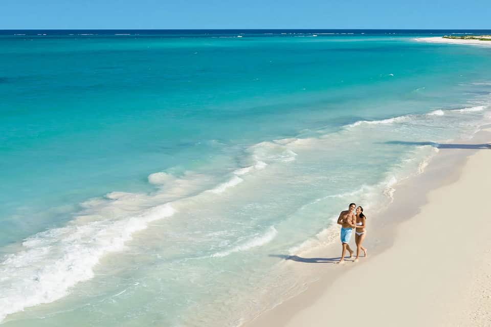 Couple walking on pristine white sand beach with turquoise ocean waters