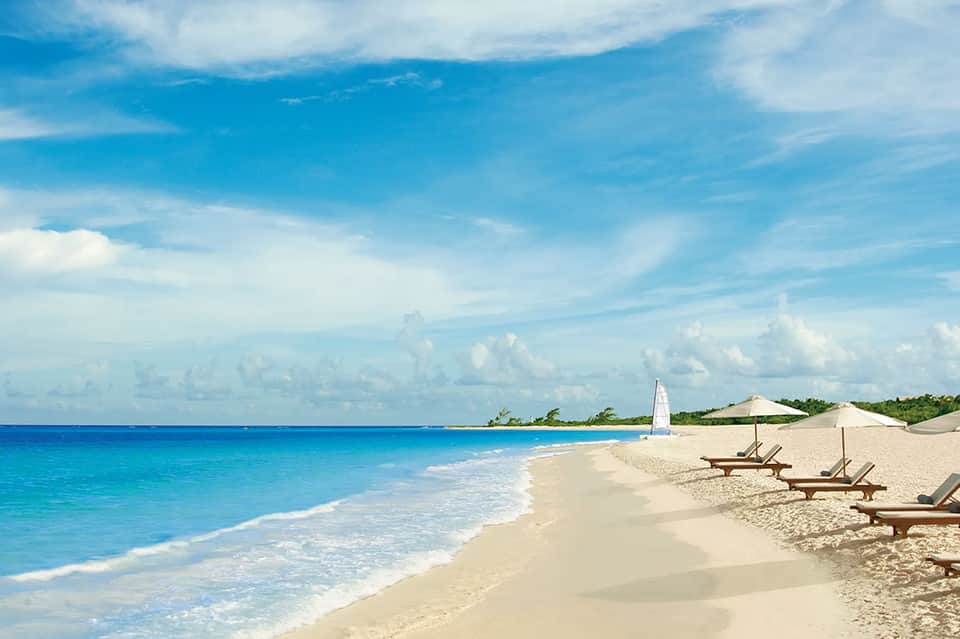 Pristine sandy beach with turquoise ocean waves, lounge chairs, and sailboat