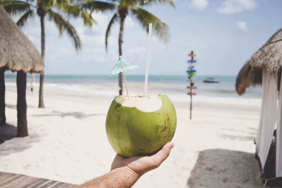 Hand holding fresh green coconut drink with umbrella on tropical beach