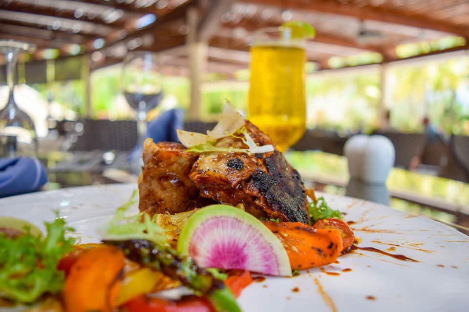 Grilled fish dish with vegetables on white plate at outdoor restaurant