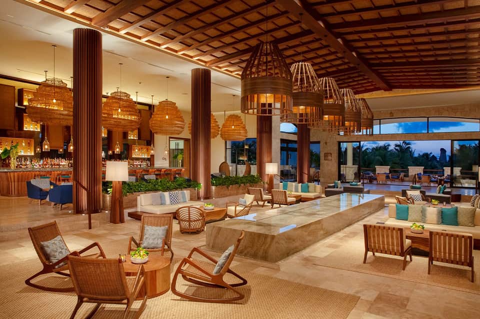 Modern resort lobby with wooden columns, woven pendant lights, and lounge seating areas