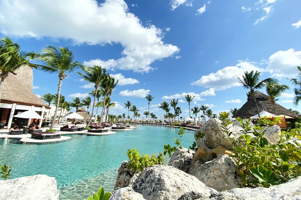 Turquoise lagoon pool with thatched-roof structures and palm trees in tropical resort setting