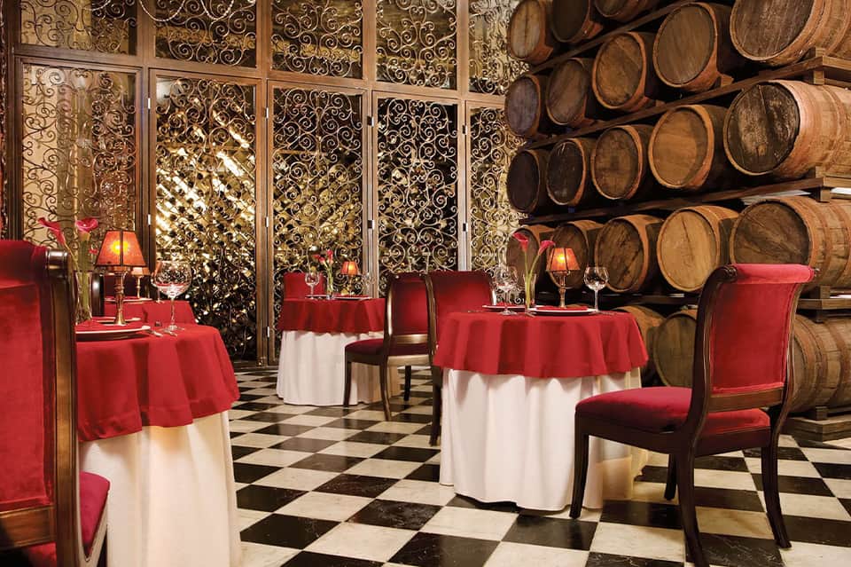 Elegant dining room with red tablecloths, ornate gold screens, and wine barrel display