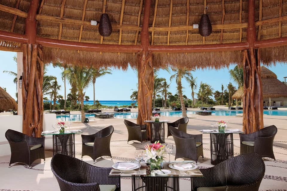 Thatched gazebo dining area with wicker chairs overlooking pool and palm landscape