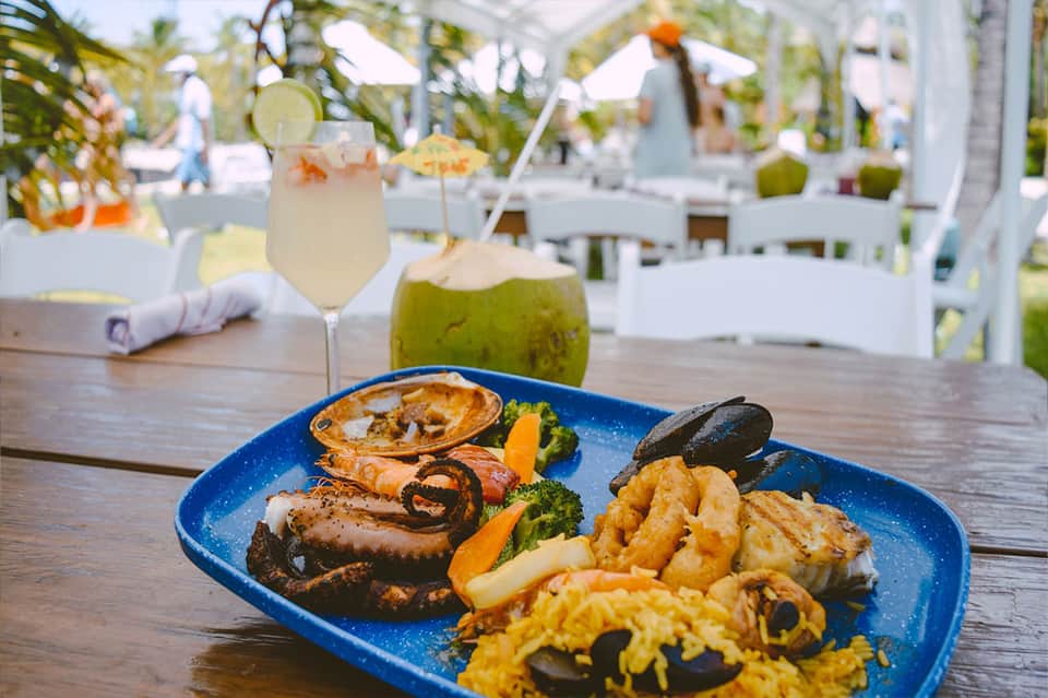 Beachfront dining table with fresh seafood platter, tropical cocktails, and ocean view in background