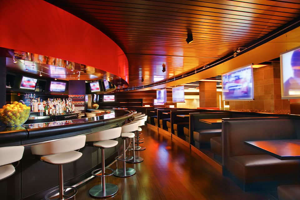 Modern lounge bar with curved red and orange ceiling, bar seating, and flat-screen TVs