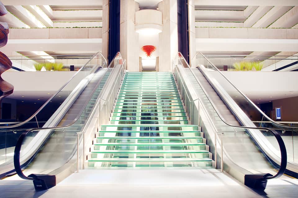 Modern mall staircase with glass steps, escalators, and red hanging art installation