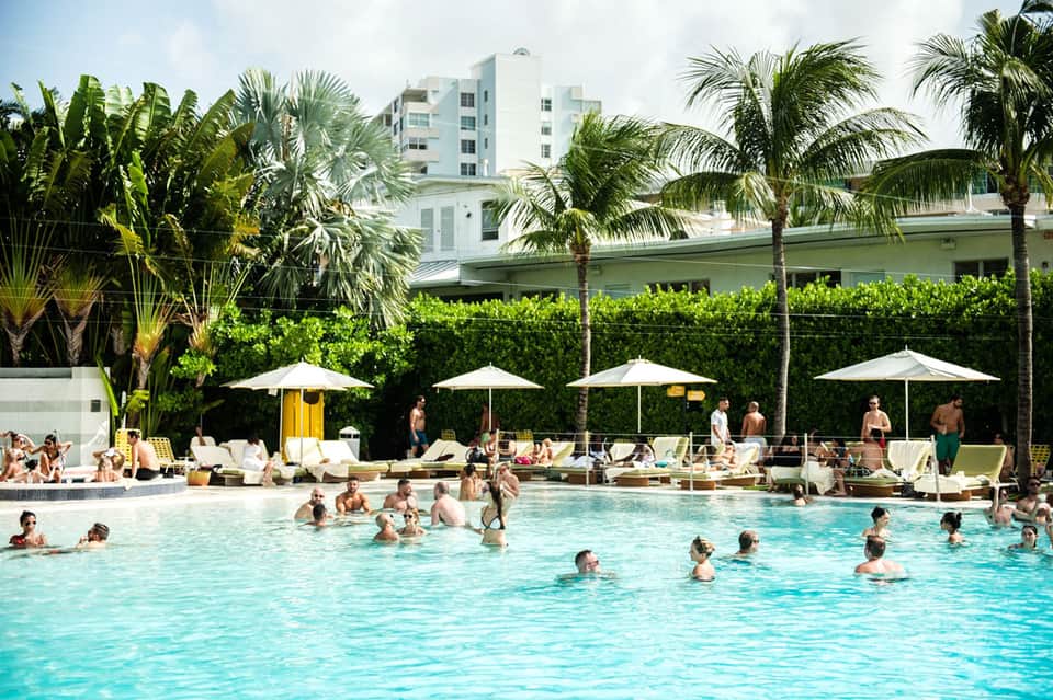 Luxury resort pool with tropical palm trees, umbrellas, and white buildings
