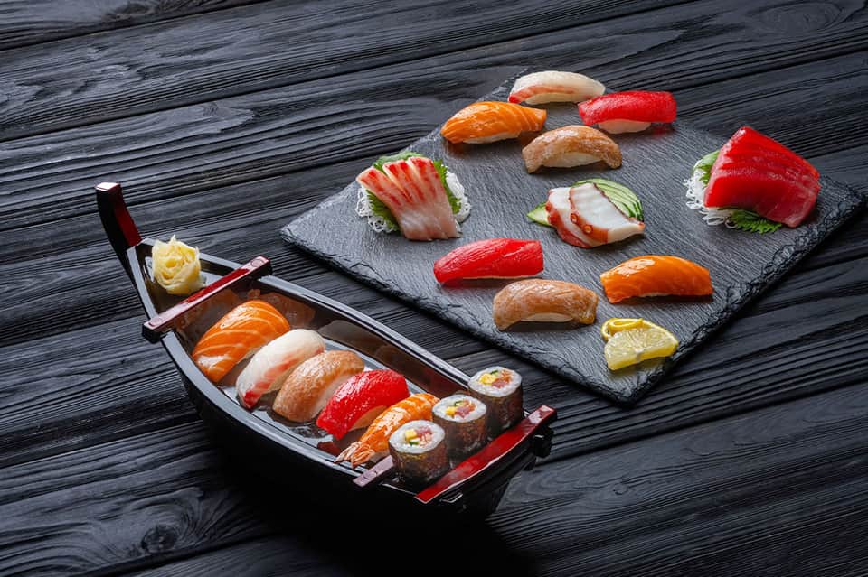 Assorted nigiri and sashimi sushi on black slate board and boat-shaped platter