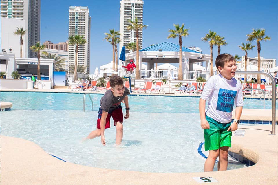 Children playing in shallow pool with palm trees and high-rise resort buildings