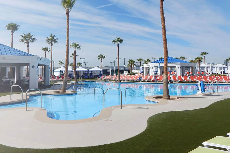 Modern resort pool with palm trees, lounge chairs, and white cabanas under blue sky