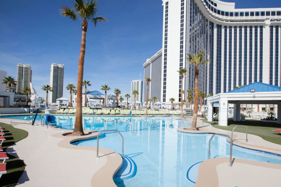 Resort pool with palm trees and tall hotel buildings under clear blue sky