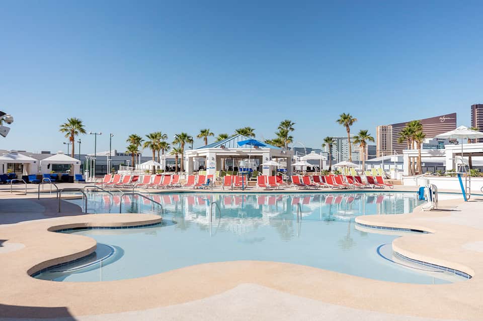 Resort pool with red lounge chairs, palm trees, and high-rise buildings in background