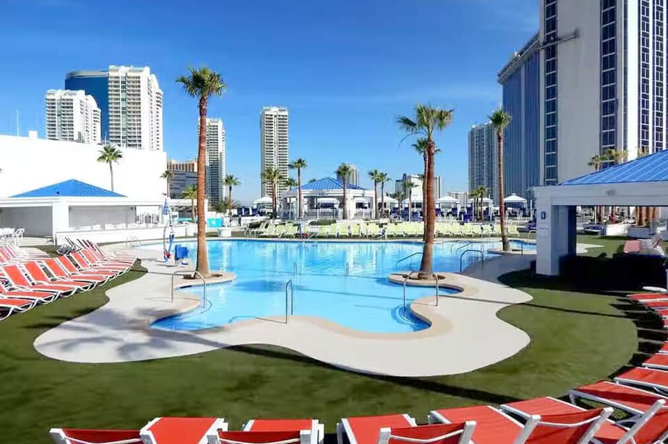 Beach resort pool with red loungers, palm trees, and high-rise hotels in background