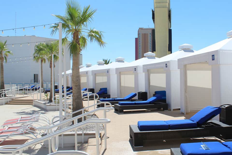 Beach cabanas with white canvas covers and blue cushioned lounges along sandy shoreline
