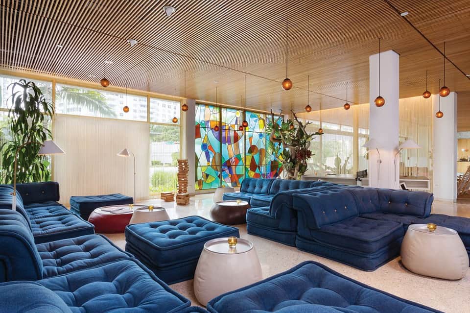 Contemporary lobby lounge with blue modular seating, stained glass window, and hanging amber lights