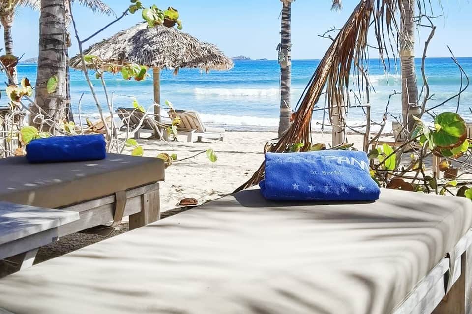 Beachfront dining cabanas with thatched umbrellas, blue cushions, and ocean view