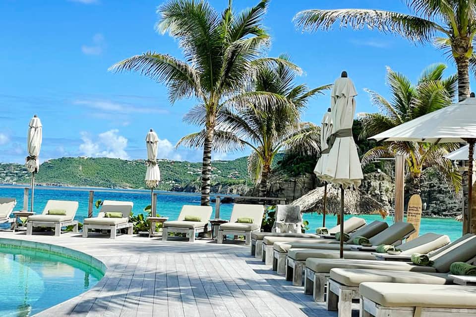Luxury resort pool deck with ocean view, lounge chairs, palm trees, and white umbrellas