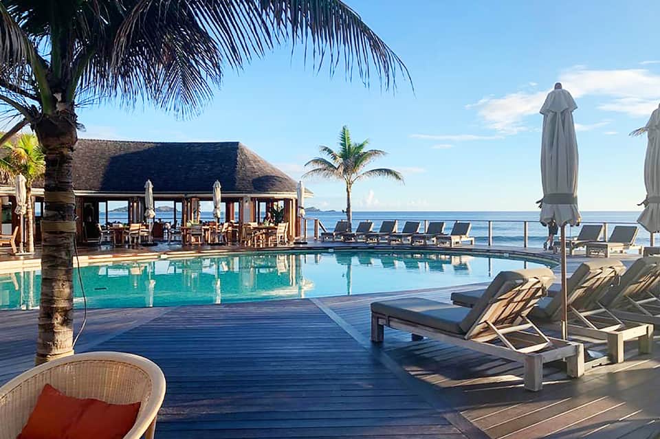 Luxury beachfront resort pool with tiki bar, ocean view, and palm trees at sunset