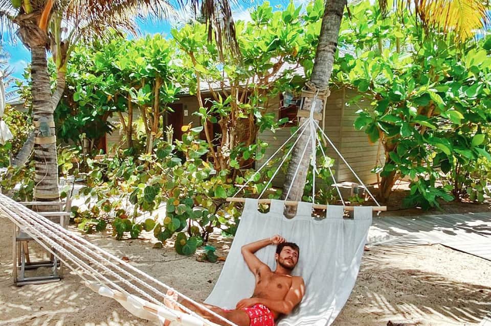 Man relaxing in white hammock under palm trees in tropical backyard setting