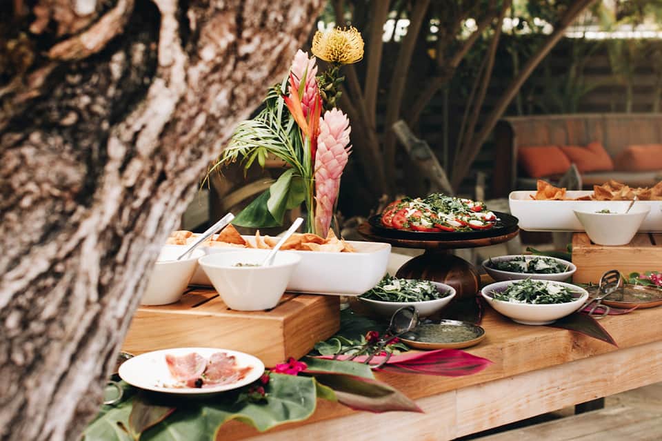 Outdoor dining table with tropical flowers, fresh salads, and appetizers on wood surface