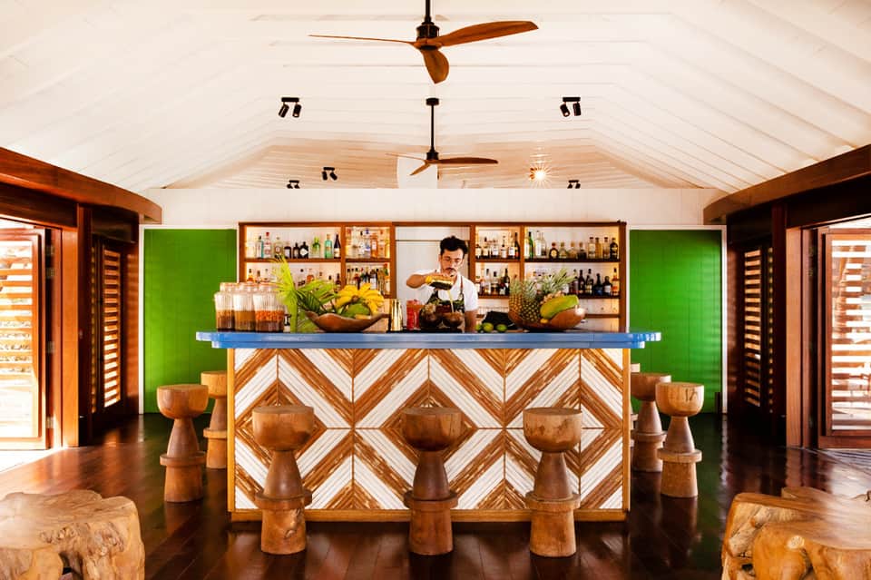 Modern tropical bar with geometric wood pattern, green walls, and bright blue counter