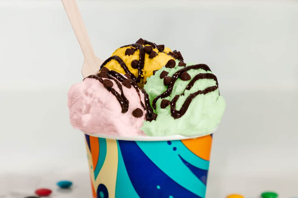 Colorful ice cream cup with three flavors and chocolate drizzle