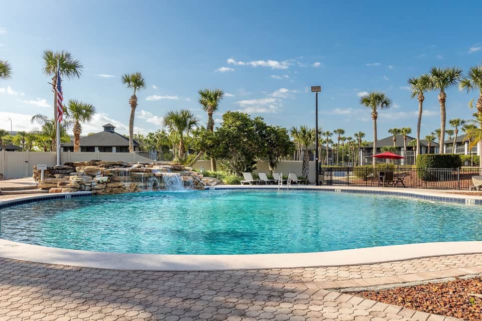 Lagoon-style pool with rock waterfall feature, surrounded by palm trees and manicured grounds